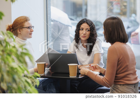 three female colleagues or students are working on a laptop and discussing a project or creative term paper. three female friends in coworking work online in an intranet 91018326