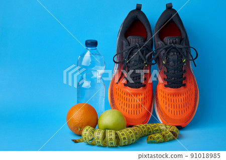 Orange sneakers, measuring tape, water botlle and fruits apples and oranges on a blue background Orange sneakers, measuring tape, water botlle and fruits apples and oranges on a blue background 91018985