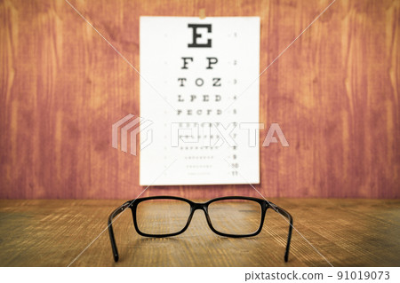 Glasses on wooden table against eye test chart Glasses on wooden table against eye test chart 91019073