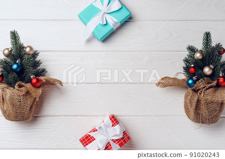 Pine tree decorated with baubles and wrapped Christmas gifts on white wooden background Pine tree decorated with baubles and wrapped Christmas gifts on white wooden background 91020243