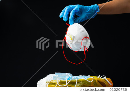 Hand putting used dirty surgical mask to a garbage bin. 91020786