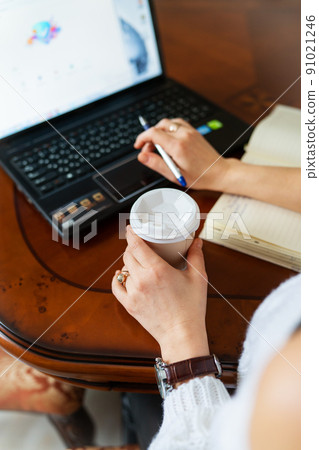 Young woman working on a laptop at home at the table, online learning on PC, e-learning. Work online, remote work. Close-up view over the shoulder. 91021246