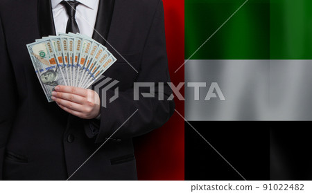 Hand giving 100 US dollar bills money banknotes against flag of United Arab Emirates background 91022482