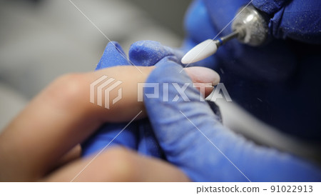 Manicurist doing hardware manicure to female client using special apparatus 91022913