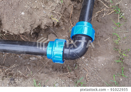 Elbow fitting and pvc pipes at bend in dirt trench outdoors 91022935