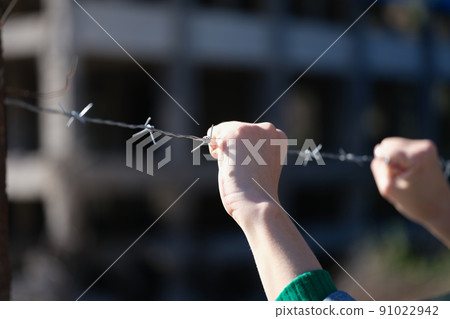 Woman hands holding metal security barbedwire fence Woman hands holding metal security barbedwire fence 91022942