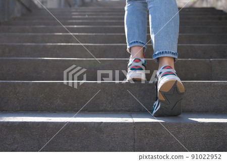 Female in jeans and sneakers going up steep stairs Female in jeans and sneakers going up steep stairs 91022952
