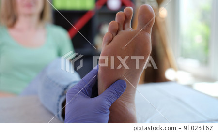 Doctor podiatrist in sterile gloves examining female foot 91023167