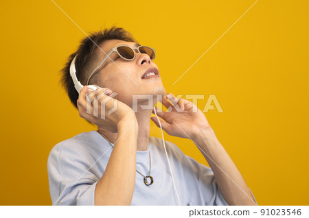 A man wearing sunglasses and listening to music on headphones A man wearing sunglasses and listening to music on headphones 91023546