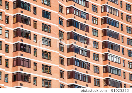 View of brick wall red contemporary apartment building with windows and balconies closeup 91025253