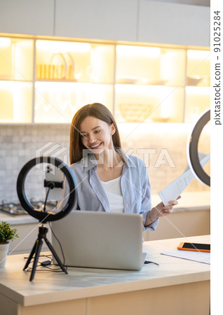 Thoughtful woman smiling at laptop holding document 91025284