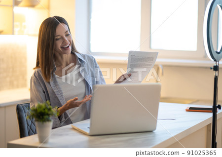 Woman pointing at papers smiling at laptop 91025365