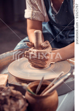 The potter works in the workshop. Hands and a potter's wheel close-up The potter works in the workshop. Hands and a potter's wheel close-up 91025767
