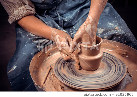 Craftsman siting on bench with pottery wheel and making clay pot. National craft. Close-up. 91025905