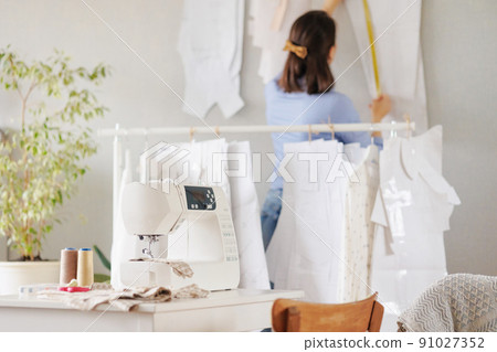 woman sews clothes on a sewing machine in a workshop. work in the production of clothing and textiles. patterns and fabrics for sewing woman sews clothes on a sewing machine in a workshop. work in the production of clothing and textiles. patterns and fabrics for sewing 91027352