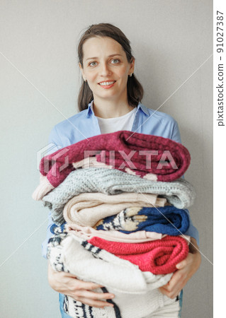 woman holds colored sweaters and clothes in her hands. washing and care of clothes, powder and conditioner for washing. a happy woman stylist woman holds colored sweaters and clothes in her hands. washing and care of clothes, powder and conditioner for washing. a happy woman stylist 91027387