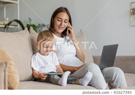 mom and son at home in the living room. parenting and business for a young European mom. A woman is working on a laptop and playing with her son 91027393