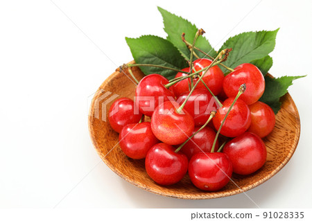 Cherry on a wooden plate with leaves on a white background 91028335