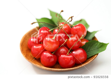 Cherry on a wooden plate with leaves on a white background 91028338