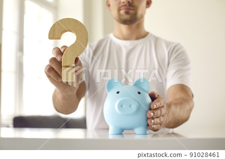 Man who is thinking about what currency to keep money holds question mark near piggy bank. Man who is thinking about what currency to keep money holds question mark near piggy bank. 91028461