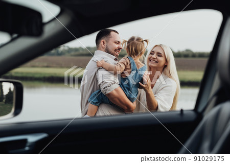 View Through Window Inside of Car, Happy Young Family with Kid Hugging Together and Enjoying Weekend Outside the City 91029175