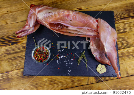 Whole raw rabbit meat with spices on a black slate cutting board on wooden table. Top view 91032470