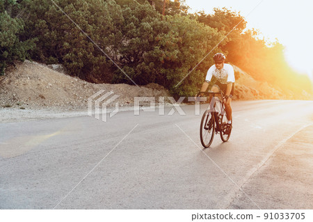 Man cyclist pedaling on a road bike outdoors in sun set Man cyclist pedaling on a road bike outdoors in sun set 91033705