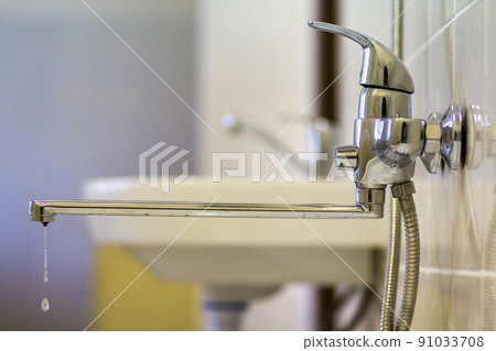 Water tap, chrome stainless metal faucet with running water stream connected to shower stall tiled wall, mixer cold hot water on blurred bathroom background. Modern home interior. 91033708