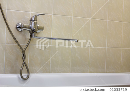 Water tap, chrome stainless metal faucet connected to shower stall tiled wall, mixer cold hot water on blurred bathroom copy space background. Modern home interior. Water tap, chrome stainless metal faucet connected to shower stall tiled wall, mixer cold hot water on blurred bathroom copy space background. Modern home interior. 91033719