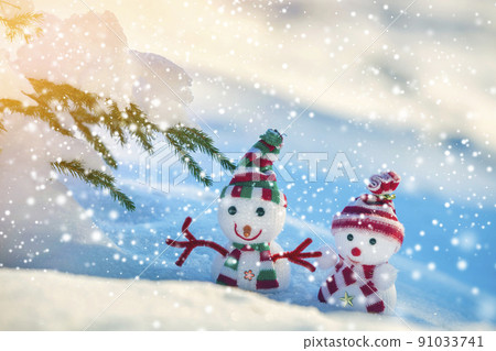 Two small funny toys baby snowman in knitted hats and scarves in deep snow outdoors on bright blue and white copy space background. Happy New Year and Merry Christmas greeting card. Two small funny toys baby snowman in knitted hats and scarves in deep snow outdoors on bright blue and white copy space background. Happy New Year and Merry Christmas greeting card. 91033741