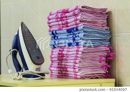 Ironing linen with steam generator. A stack of ironed towels lying next to the iron. Teflon sole plate covered with small holes. 91034097