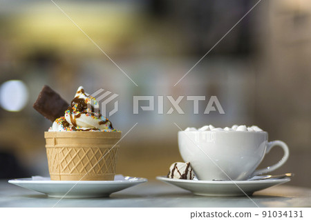 Ice cream dessert in wafer cup with chocolate cookies and and mug of coffee with marshmallows on porcelain plate on blurred colorful copy space background. 91034131