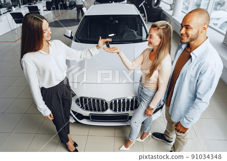 Car saleswoman in a car dealership having a talk with clients Car saleswoman in a car dealership having a talk with clients 91034348