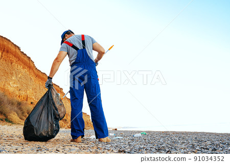 Man volunteer collecting garbage on the beach with a reach extender stick Man volunteer collecting garbage on the beach with a reach extender stick 91034352