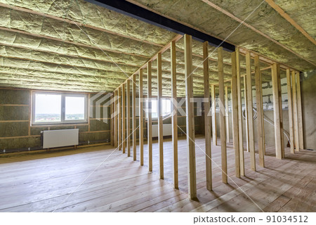 Construction and renovation of big light spacious empty room with oak floor, walls and ceiling insulated with rock wool, heating radiators under low attic windows and wooden frame for future walls. 91034512
