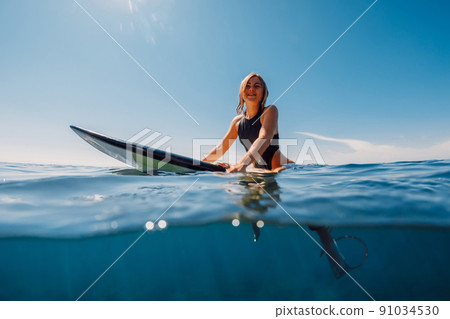 Attractive surf girl sit on surfboard in ocean. 91034530