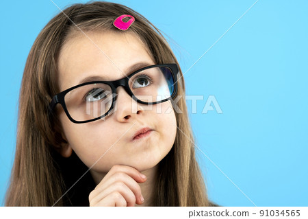 Close up portrait of a child school girl wearing looking glasses holding hand to her face thinking about something isolated on blue background. 91034565