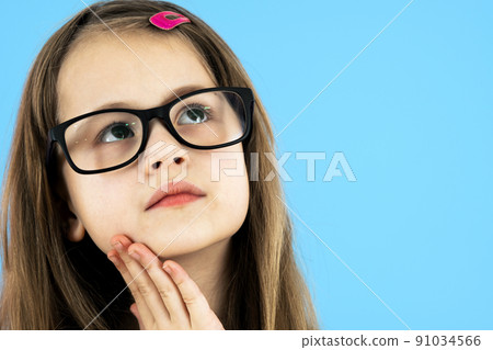 Close up portrait of a child school girl wearing looking glasses holding hand to her face thinking about something isolated on blue background. Close up portrait of a child school girl wearing looking glasses holding hand to her face thinking about something isolated on blue background. 91034566