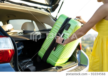Close up of woman taking green suitcase from car trunk. Travel and vacations concept. Close up of woman taking green suitcase from car trunk. Travel and vacations concept. 91034568