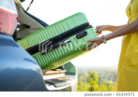 Close up of woman hands taking green suitcase from car trunk. Travel and vacations concept. Close up of woman hands taking green suitcase from car trunk. Travel and vacations concept. 91034571