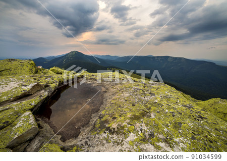 Blue sky reflected in small lake on rocky mountain peak on blue mountain range background at dawn. Blue sky reflected in small lake on rocky mountain peak on blue mountain range background at dawn. 91034599