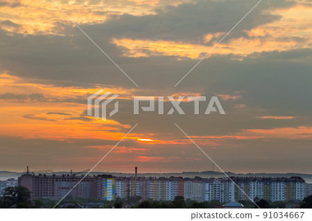 Beautiful bright orange sky at sunset over high apartment building, working tower cranes and houses roofs among green trees on distant mountain background. Construction and real property concept. Beautiful bright orange sky at sunset over high apartment building, working tower cranes and houses roofs among green trees on distant mountain background. Construction and real property concept. 91034667