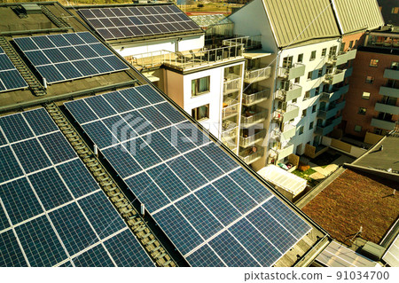 Aerial view of solar photovoltaic panels on a roof top of residential building block for producing clean electric energy. Autonomous housing concept. Aerial view of solar photovoltaic panels on a roof top of residential building block for producing clean electric energy. Autonomous housing concept. 91034700