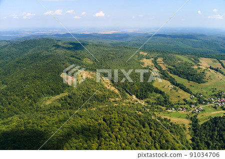 Aerial view of mountain hills covered with dense green lush woods on bright summer day. 91034706