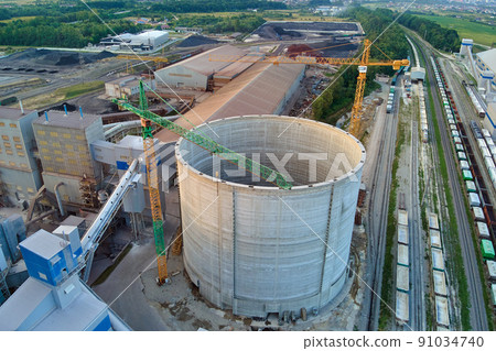Aerial view of cement factory under construction with high concrete plant structure and tower cranes at industrial production area. Manufacture and global industry concept. Aerial view of cement factory under construction with high concrete plant structure and tower cranes at industrial production area. Manufacture and global industry concept. 91034740
