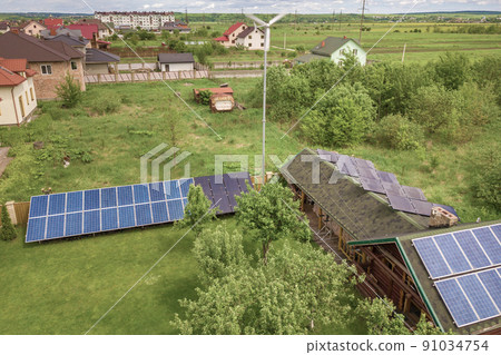 Aerial view of a residential private house with solar panels on roof and wind generator turbine. Aerial view of a residential private house with solar panels on roof and wind generator turbine. 91034754