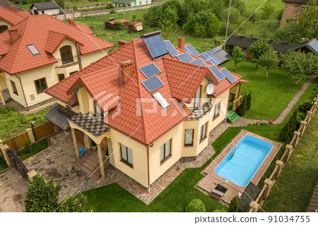 Aerial view of a new autonomous house with solar panels and water heating radiators on the roof and green yard with blue swimming pool. Aerial view of a new autonomous house with solar panels and water heating radiators on the roof and green yard with blue swimming pool. 91034755