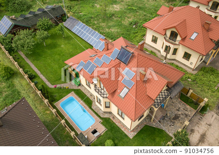 Aerial view of a new autonomous house with solar panels and water heating radiators on the roof and green yard with blue swimming pool. 91034756