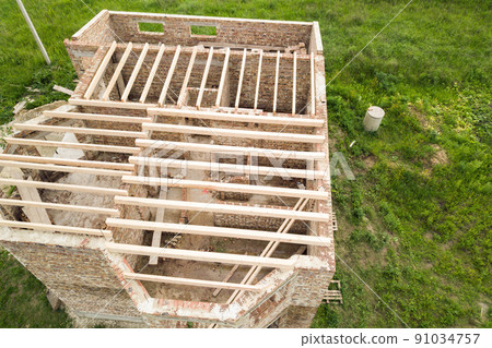Aerial view of a brick house with wooden ceiling frame under construction. 91034757