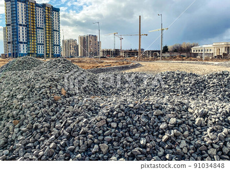 construction of a new microdistrict in the city center. tall, high-rise buildings made of concrete and glass next to a pile of stones. gray stones lie for the construction of the road 91034848